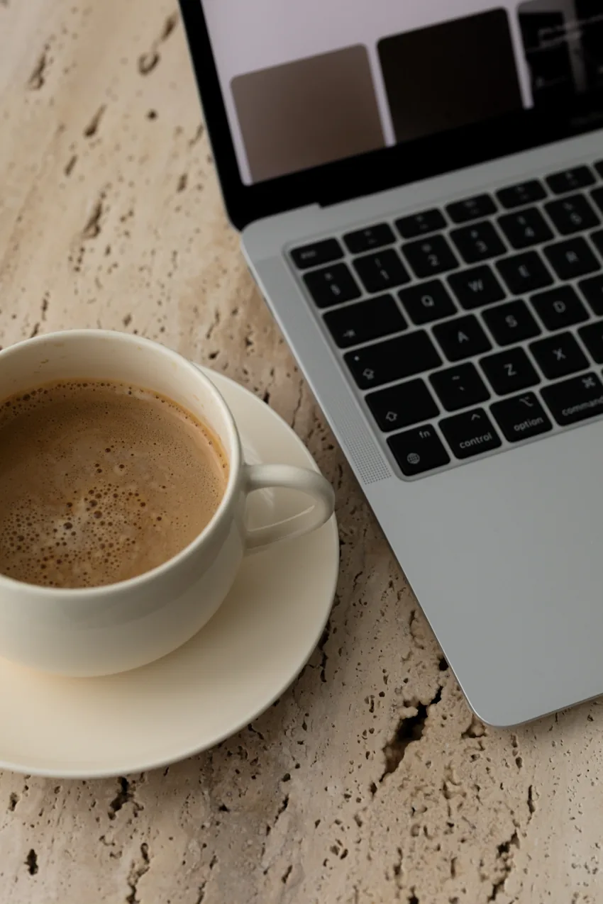 Un café et un ordinateur sur une table en pierre claire.