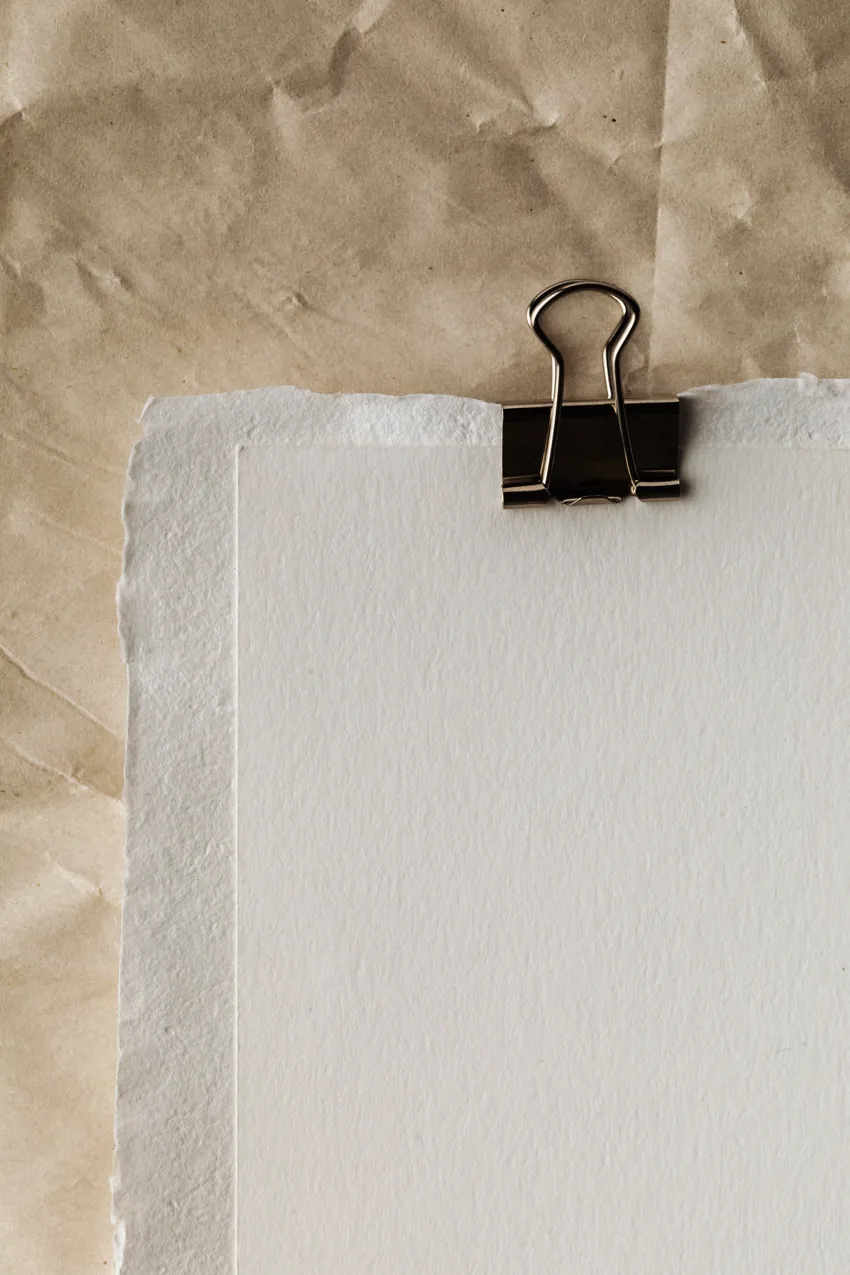 Des feuilles de papier maintenues par une pince sur un fond kraft.